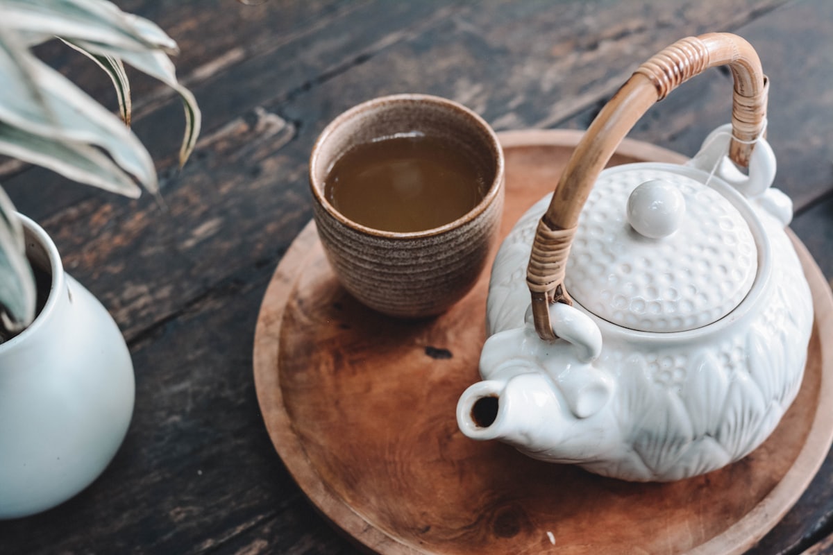 Kanne und Schale mit frisch aufgegossenem Kräutertee auf einem Holztablett